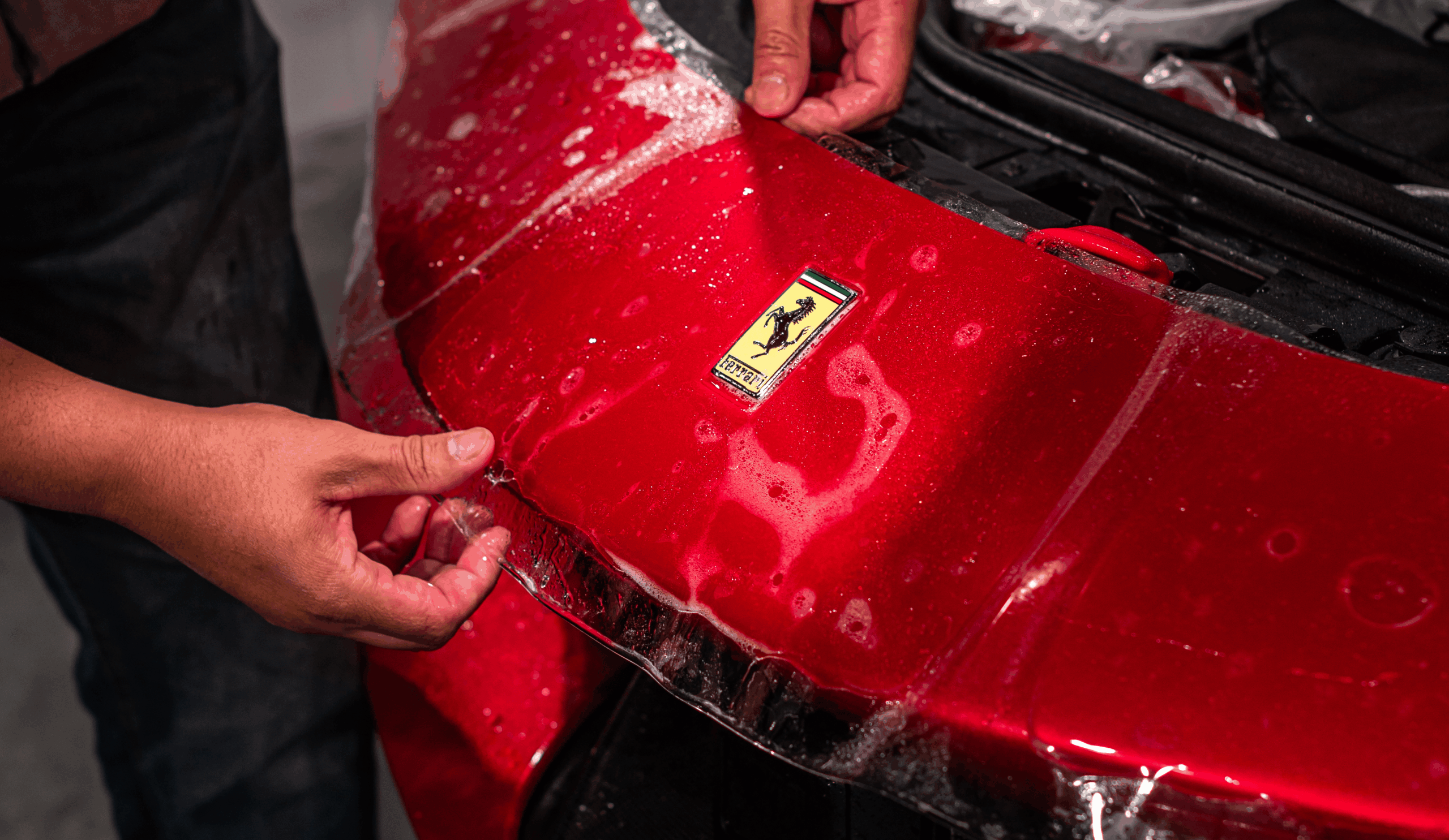 Applying clear paint protection film on red Ferrari hood at TintProsNJ in Monmouth County